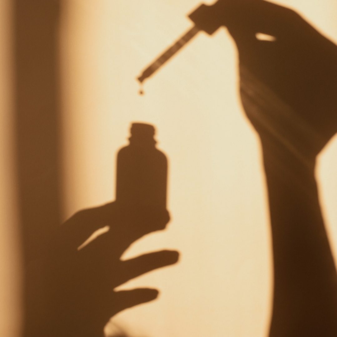 A hand holding a dropper above a bottle, cast in shadow