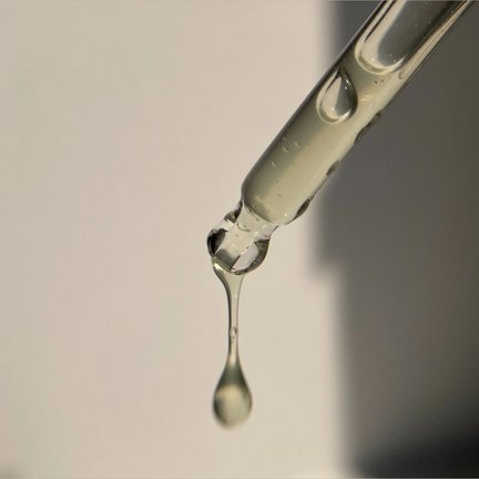 A single drop of oil falling from a glass dropper